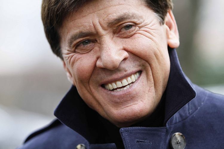 Gianni Morandi sorridente davanti a un fotografo